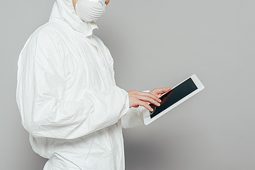 cropped view of epidemiologist in hazmat suit and respirator mask holding digital tablet with blank screen on grey background