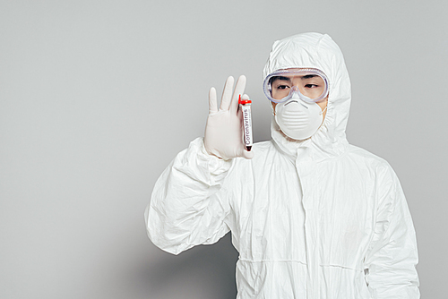 asian epidemiologist in hazmat suit and respirator mask showing test tube with blood sample on grey background