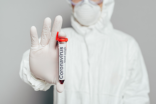 selective focus of epidemiologist in hazmat suit showing test tube with blood sample on grey background