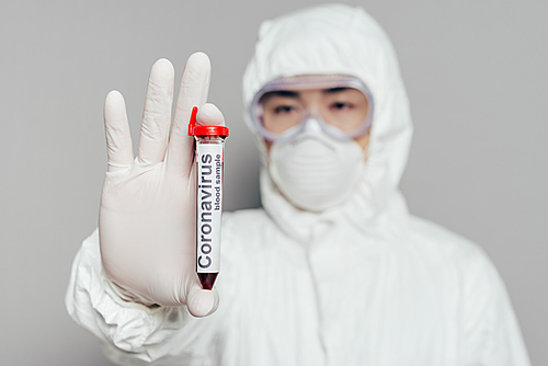 selective focus of asian epidemiologist in hazmat suit and respirator mask showing test tube with blood sample on grey background