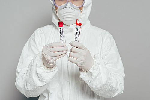 cropped view of epidemiologist in hazmat suit and respirator mask holding test tubes with blood samples on grey background