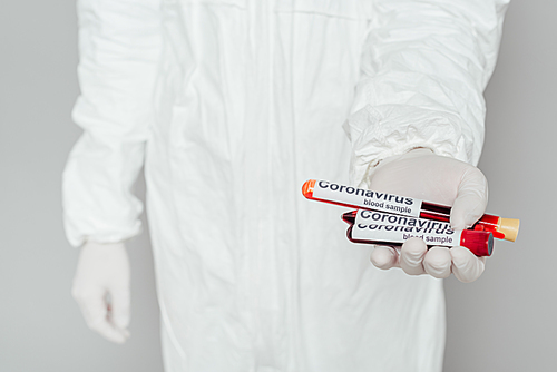 partial view of epidemiologist in hazmat suit showing test tubes with blood samples on grey background