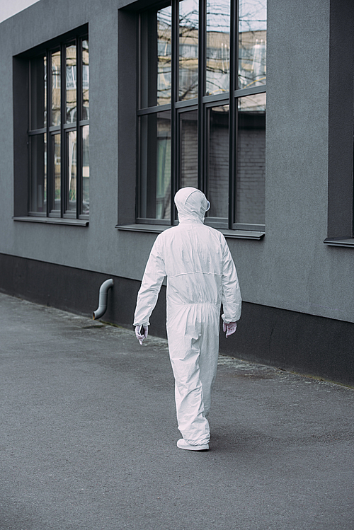 back view of epidemiologist in hazmat suit walking along building