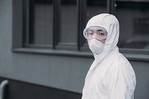 asian epidemiologist in hazmat suit and respirator mask  while standing on street