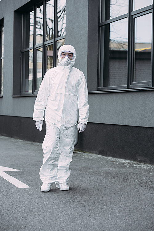 asian epidemiologist in hazmat suit and respirator mask  while standing on street near building