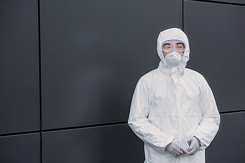 asian epidemiologist in hazmat suit and respirator mask  while standing near wall