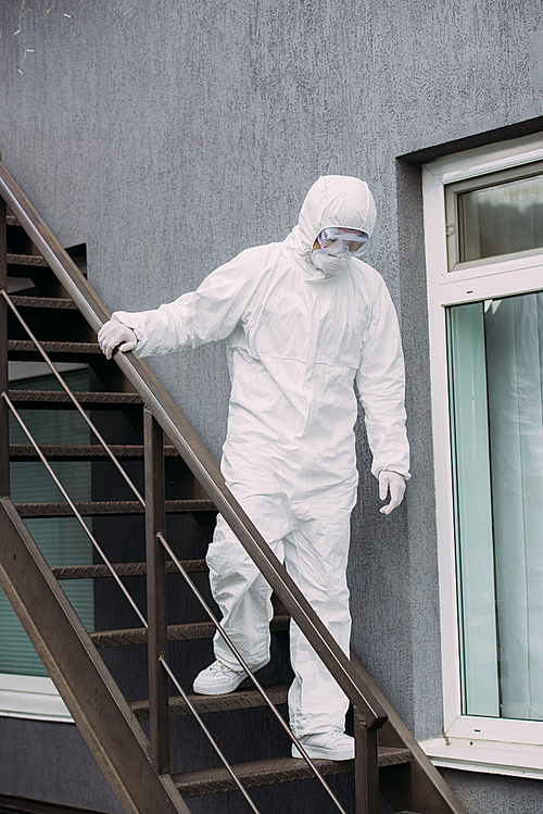 asian epidemiologist in hazmat suit and respirator mask walking downstairs outside building