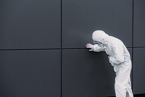 asian epidemiologist in hazmat suit leaning on wall while suffering from symptomatic abdominal pain