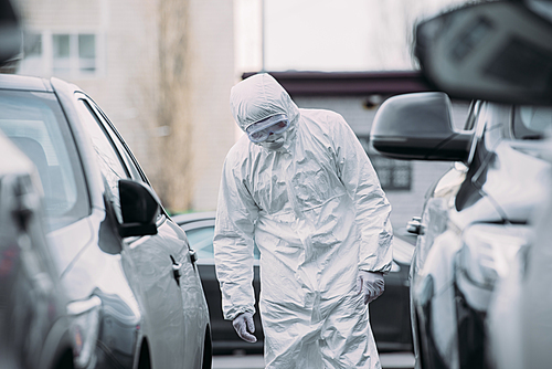 selective focus of asian epidemiologist in hazmat suit and respirator mask inspecting vehicles on parking lot