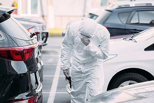 asian epidemiologist in hazmat suit and respirator mask inspecting vehicles on parking lot