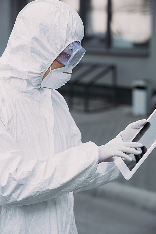 asian epidemiologist in hazmat suit and respirator mask using digital tablet while standing on street