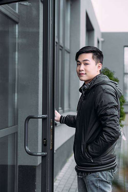 young asian man  while standing near building and opening door