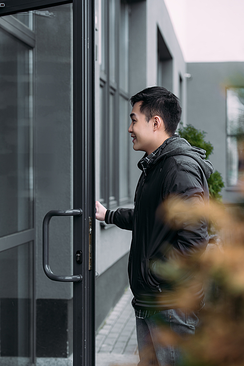 selective focus of young asian man smiling while opening door and entering building