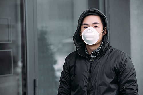 young asian man in respirator mask  while standing on street