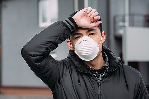 young asian man in respirator mask  while suffering from headache and touching forehead