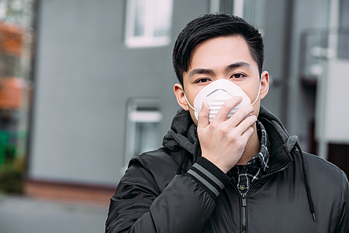 young asian man touching respirator mask and  while standing on street