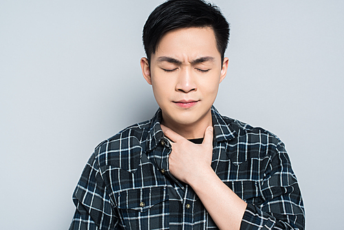 young asian man with closed eyes touching neck while suffering from sore throat isolated on grey