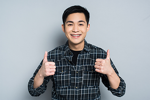 smiling asian man  while showing thumbs up on grey background