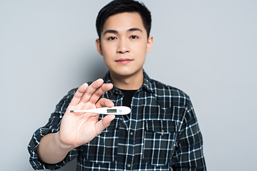 selective focus of young asian man holding thermometer while  on grey background