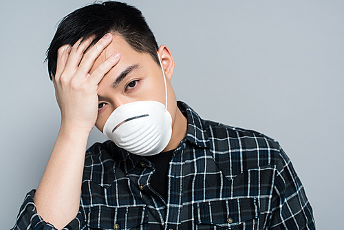 young asian man in respirator mask touching forehead and  while suffering from headache isolated on grey