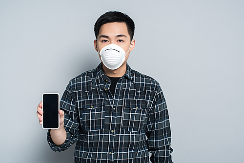 young asian man in respirator mask showing smartphone with blank screen and  on grey background