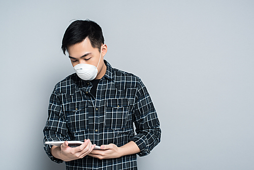 young asian man in respirator mask using digital tablet on grey background