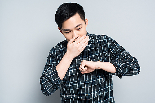 young asian man covering mouth while coughing on grey background