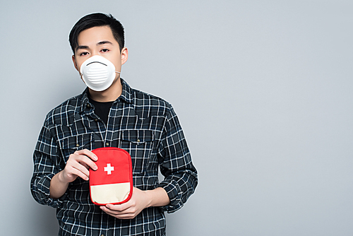 young asian man in respirator mask showing first aid kit while  isolated on grey