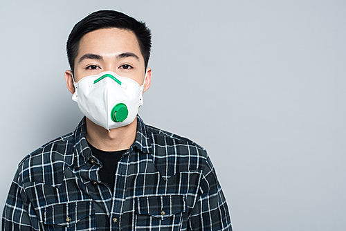 young asian man in respirator mask  while standing isolated on grey
