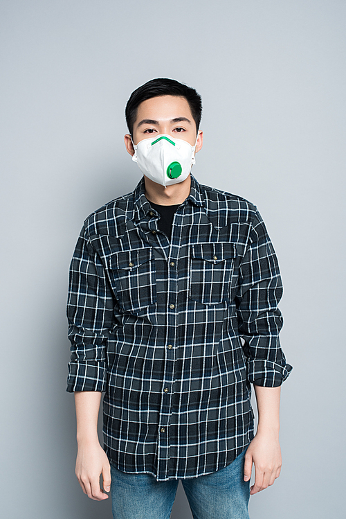 young asian man in respirator mask  while standing on grey background