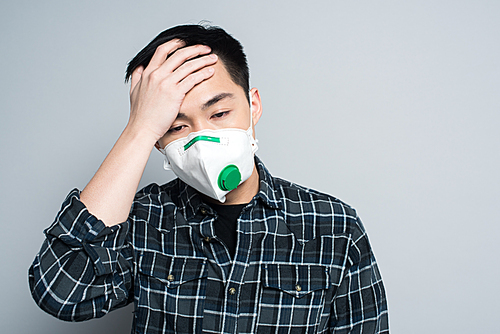 young asian man in respirator mask touching forehead while suffering from headache on grey background