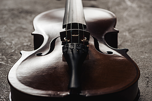 close up of classical wooden cello on grey textured background in darkness