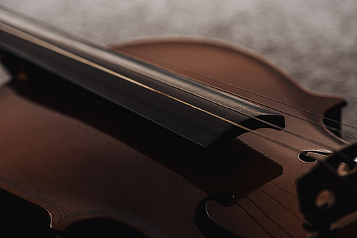 close up of strings on wooden violoncello in darkness on grey textured background