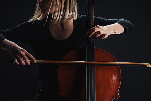 cropped view of young woman playing double bass in darkness isolated on black