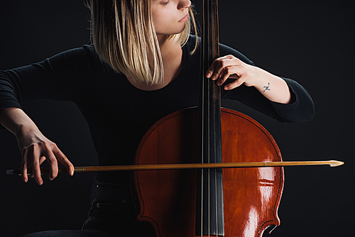 partial view of tattooed woman playing double bass in darkness isolated on black