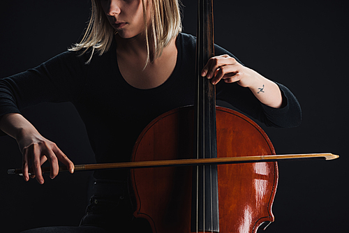 cropped view of tattooed woman playing double bass in darkness isolated on black