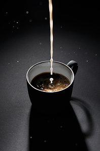 Cup of coffee with pouring milk on dark textured surface