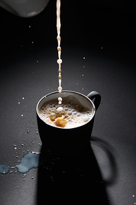 Cup of coffee with pouring milk on dark textured surface