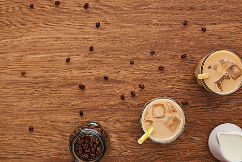 top view of ice coffee in glasses with straw, milk and coffee grains on wooden table