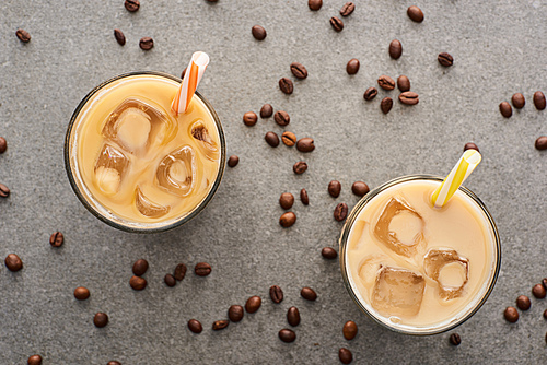 top view of ice coffee with straws and coffee grains on grey background