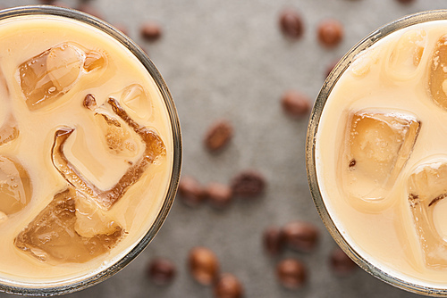 close up view of ice coffee in glasses with coffee grains on grey background