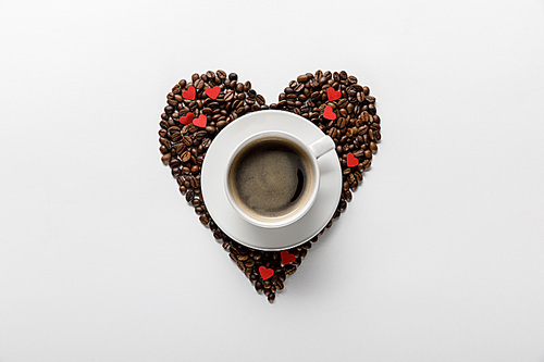top view of coffee in cup on saucer with heart made of coffee grains on white background