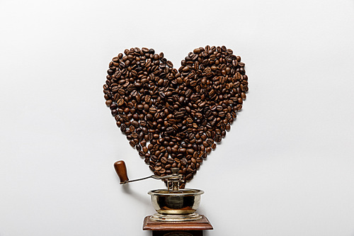 top view of heart made of coffee grains near vintage coffee grinder on white background