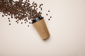 top view of coffee to go and scattered fresh coffee beans on beige background