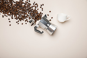 top view of aluminium coffee pot, cup and fresh coffee beans on beige background