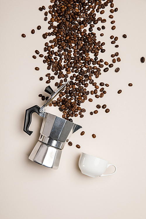top view of aluminium coffee pot, cup and scattered fresh coffee beans on beige background