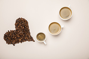 top view of cups with coffee near heart made of coffee grains on beige background