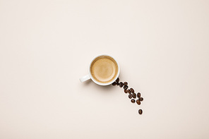 top view of cup with tasty coffee near coffee grains on beige background