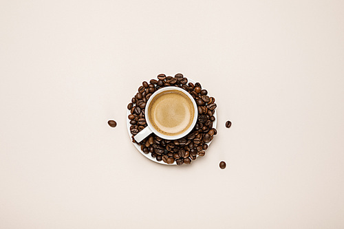 top view of cup with delicious coffee on coffee grains on beige background