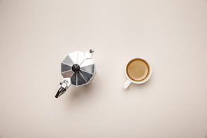 top view of metal coffee pot and delicious coffee in cup on beige background